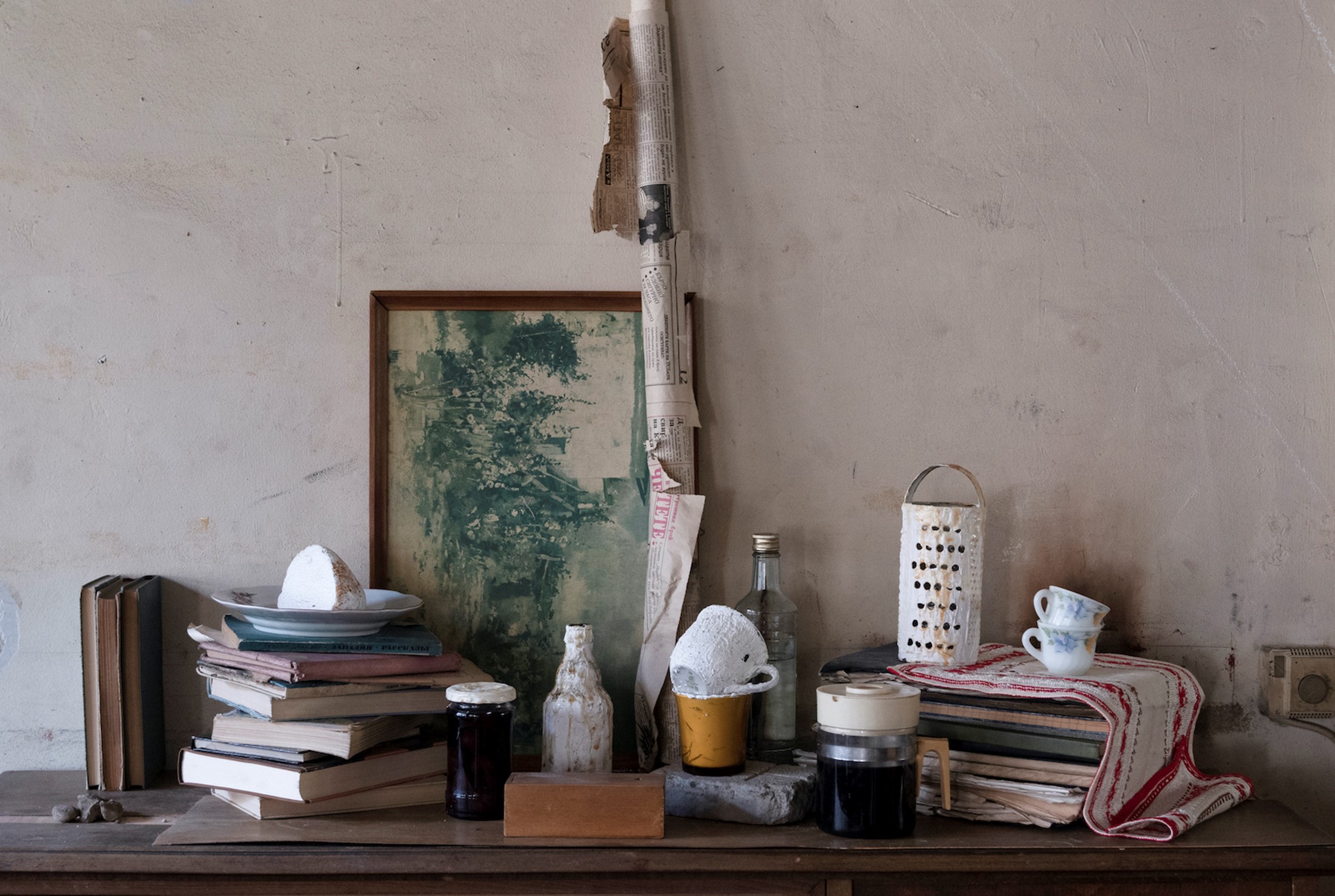 Table piled with a variety of well used items like books, cups, bottles, and newspaper.