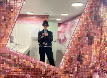 T.L. Cowan poses for a selfie in a bathroom mirror. The bathroom is in the Helsinki Art Museum, and features the mosaic “You don’t know how beautiful you are” by the artist Tuula Lehtinen. 
